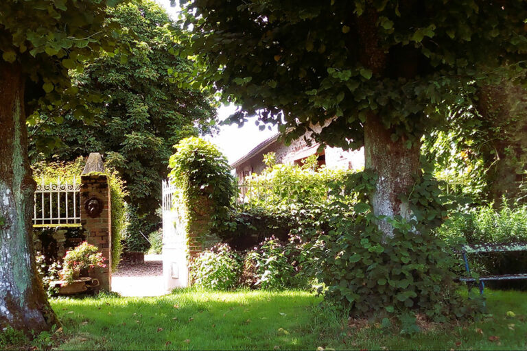 Une porte ouverte sur un chemin menant vers une maison de campagne entourée de jardin